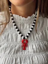 Collar de cuentas redondas negras y blancas con dije de langosta roja.