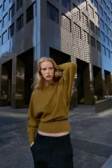Jersey de punto color mostaza con cuello barco, manga larga con sisa ancha y detalle de cinturón fino integrado en la cintura.