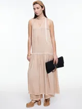 Vestido largo de viscosa en tono beige con efecto gastado, diseño sin mangas con escote halter y tira tipo choker para anudar al cuello. Presenta un corte a la altura de la cadera con falda amplia y fruncida que aporta movimiento y caída fluida.