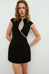 Vestido corto negro con cuello mao, abertura en el pecho y ribetes blancos en contraste. Cuenta con mangas cortas y cierre lateral con cremallera oculta.