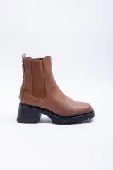 Botas de caña media color marrón de cuero sintético con paneles elásticos laterales, suela track negra con plataforma y taco, y detalle de tachas metálicas en la parte trasera.