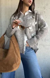 Cardigan de punto color beige con diseño de flores bordadas en relieve, cuello redondo, cierre frontal con botones y puños acanalados.