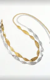 Cinto de cadena dorado, estilo body chain, compuesto por eslabones metálicos con forma de hoja alargada y textura martillada. Se ajusta a la cintura.