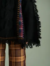 Sweater oversize de lana con diseño de trenza central, detalles en tejido cuadrillé y terminaciones desflecadas. Presenta mangas acampanadas, cuello a la base y aberturas laterales con tiras ajustables.