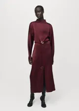 Vestido midi de tejido satinado en color bordó, con cuello alto, manga larga y diseño recto. Presenta una abertura frontal en el bajo y un cinturón ajustable con detalle metálico en la cintura.