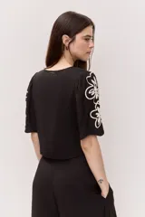Blusa corta de color negro con escote en V, mangas cortas y bordados florales en contraste sobre las mangas.