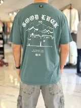 Remera oversize verde con estampado gráfico en la espalda con diseño de paisaje oriental y texto.