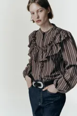 Camisa de manga larga con cuello subido, cierre frontal con botones y detalle de volantes en el pecho. Presenta un diseño a rayas verticales y puños elásticos.