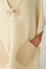 Chal de lana fina sin teñir con diseño de cuadros sutiles, cierre frontal con alamar y bolsillos de cuero metalizado. Presenta terminaciones con flecos en el ruedo y un calce estructurado en los hombros.