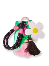 Llavero de muñeca con cordón trenzado negro con detalles en rosa, que incluye un porta tarjeta de acrílico verde, un dije de flor blanca con centro amarillo, una borla rosa y una borla marrón.