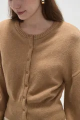 Saco de punto color beige, con cuello redondo, cierre frontal con botones y mangas largas con puños acanalados.