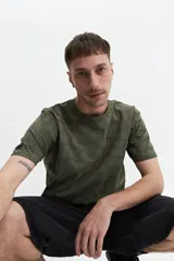 Remera verde militar con estampado de hojas en tono más oscuro, de manga corta, cuello redondo y corte regular.