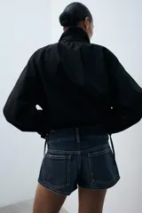 Cazadora de algodón negra con cuello subido ajustable con lazadas, manga larga, bolsillos de vivo en los laterales y bajo ajustable con cordones. Cierre frontal con botones.