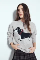 Sweater de punto color gris melange con diseño tejido de un perro salchicha en el frente. Presenta cuello redondo, mangas largas y un corte relajado.
