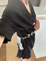 Cinturón de cuero negro con hebilla plateada y riñonera plateada con flecos.