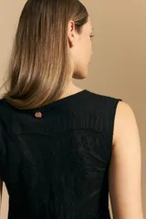 Top sin mangas de jacquard color negro, con cuello cerrado y silueta recta. Presenta una textura trabajada con relieve y una terminación suavemente ondulada en el ruedo.