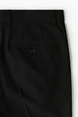 Pantalón sastrero de corte ajustado, color negro, con pliegues frontales, cierre de botón, bolsillos laterales y bolsillos traseros ribeteados.