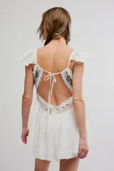 Enterito corto blanco de tela liviana, con escote en V, canesú de encaje con bordados brillantes, volados en los tirantes y diseño de short con falda con vuelo.