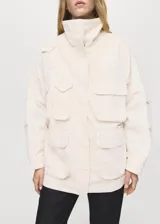 Anorak de estilo utilitario en color crudo, con cuello alto tipo embudo, cierre frontal con cremallera y botones a presión, y múltiples bolsillos de parche con solapa. Presenta un diseño oversize de manga larga.