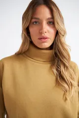 Buzo tipo polera de algodón, con cuello alto, mangas largas con puños y diseño holgado. Presenta una pequeña grifa metálica decorativa.