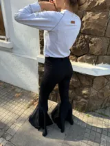 Pantalón negro de tiro alto con corte acampanado y terminación en volado en el ruedo.