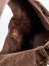 Cartera hobo de gamuza marrón, con tiras de flecos decorativos en el frente y asa integrada para llevar al hombro.
