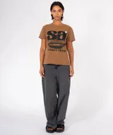 Camiseta de manga corta color gris oscuro con efecto lavado, cuello redondo y terminaciones desgastadas. Estampado frontal con las letras "Sa" en grande, una ilustración de labios con líneas verticales y el texto "SPOKEN ARTS". Incluye un pin decorativo en la zona del hombro.