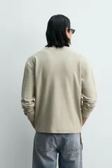 Camiseta de manga larga para hombre con corte relajado, confeccionada en tejido con estructura waffle. Presenta un cuello redondo tipo panadero con cierre frontal de botones a presión.