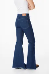 Pantalón de jean azul oscuro, corte acampanado (flare) de tiro alto, con costuras visibles en contraste y bordados tonales en la parte inferior de las piernas. El ruedo es deshilachado.