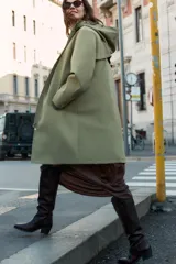 Chubasquero de acabado engomado en color verde militar, con capucha ajustable mediante cordones, cierre frontal con cremallera y botones a presión ocultos, y bolsillos laterales con solapa.
