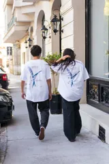 Remera blanca de algodón con estampado azul en la espalda que incluye un pájaro, texto y el logo de la marca Kangu.