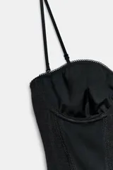 Body negro con aros y escote corazón, confeccionado con combinación de tejidos a tono, tirantes finos ajustables y cierre inferior con broches a presión.