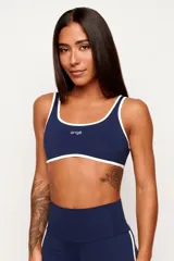 Top deportivo de poliamida color azul marino, de modelado slim y ajuste ceñido al cuerpo. Presenta escote redondo y tiras en color blanco contrastante que recorren los bordes superior e inferior, con el logo de la marca estampado en el centro del pecho.