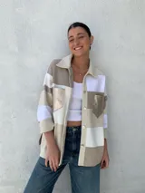 Camisa tipo chaqueta con diseño a rayas horizontales en tonos beige, blanco y marrón, con cuello camisero, cierre frontal con botones, mangas largas y bolsillos de cuero en el pecho.