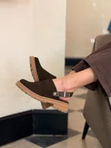 Zueco de cuero color chocolate con diseño cerrado en la parte frontal y suela de goma con plataforma baja.