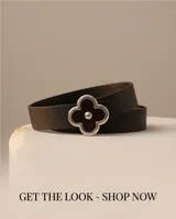 Cinto de cuero negro con hebilla plateada en forma de trébol de cuatro hojas, decorada con esmalte negro brillante y un detalle metálico esférico en el centro.