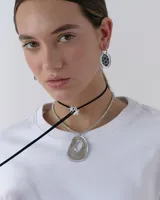 Choker tipo corbatín compuesto por un tiento de gamuza negra y un dije central en forma de flor de acrílico espejado.
