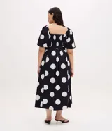 Vestido midi de algodón con estampado de lunares blancos sobre fondo negro. Presenta escote en V, mangas cortas abullonadas, cintura ajustada con cinturón de hebilla y falda con tajo lateral.