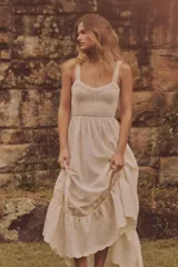 Vestido midi color crudo, con breteles anchos y escote recto. La parte superior es de tejido de punto calado y la falda es lisa con volado y detalle de puntilla en el ruedo. Tiene abertura en la espalda y cintura elastizada.