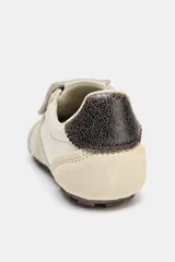 Championes deportivos de estilo minimalista en color beige, confeccionados en una combinación de materiales textiles y gamuza. Presentan una lengüeta superpuesta con cierre de gancho, punta redonda y un detalle de textura oscura en el talón. Suela plana de goma en tono marrón.