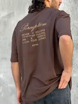 Remera marrón de corte amplio con estampado en la espalda con la palabra 'Perception' y otras frases en color dorado.