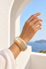 Brazalete rígido de resina con efecto marmolado en tonos dorados y traslúcidos, de diseño ancho y acabado brillante.