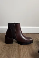 Botines de cuero vacuno en color marrón, con diseño de caña media, taco cuadrado y plataforma delantera. Presentan una combinación de texturas en el cuero y un estilo robusto.