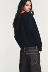 Jersey de punto de manga larga con cuello tipo polo en color naranja a contraste. Presenta cierre frontal con botones y diseño de corte holgado.