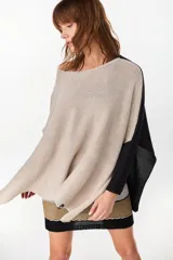 Poncho oversize de tejido de punto con aberturas laterales, cuello redondo amplio y diseño bicolor en tonos crudo y negro con detalles en lurex.