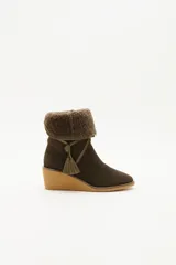 Bota de caña media color verde oliva, confeccionada en cuero con detalle de solapa superior en lana rizada. Presenta un cordón decorativo con borlas en el mismo tono y una suela de plataforma tipo cuña en color beige.