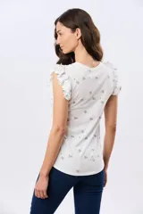 Remera blanca de algodón con estampado de ramas y pequeños frutos, escote redondo y mangas cortas con volados.