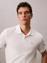 Chomba blanca de piqué de algodón, corte clásico, cuello tradicional, cartera de botones y bajo con aberturas laterales. Tiene un logo bordado en el pecho.