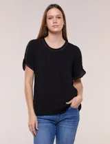 Blusa holgada de color negro, con escote redondo y mangas cortas adornadas con apliques de tachas metálicas. Presenta delicadas tablas centrales en el frente y un diseño elegante.