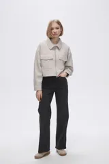 Chaqueta de eco-cuero en color beige, con diseño holgado, cuello tipo camisa y cierre frontal metálico. Presenta dos bolsillos frontales con solapa y mangas largas con puños rectos.